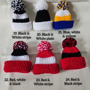 May include: Six knitted hats with pom-poms in various color combinations. The hats are black, white, blue, yellow, and red. The hats are labeled with numbers and descriptions of their color combinations. 19. Black & White stripe, 20. Black & White plain, 21. Blue, white & yellow, 22. Red, white & black, 23. Red & White stripe, 24. Red & Black stripe.