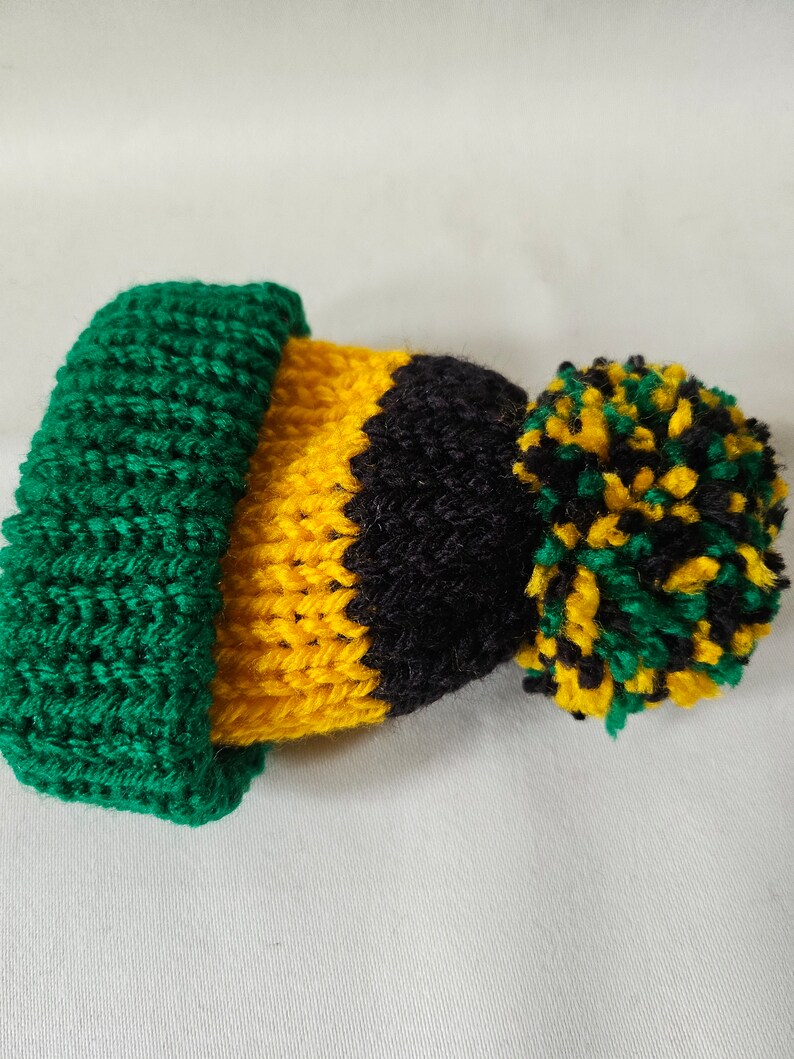 May include: A green, yellow, and black knitted hat with a pom-pom on top.