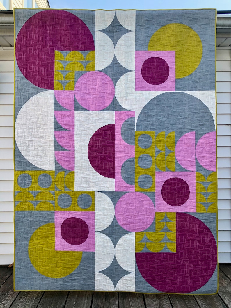 May include: A geometric quilt with a modern design. The quilt features circles, squares, and half-circles in shades of pink, purple, yellow, and gray.