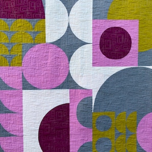 May include: A quilt with a geometric pattern in shades of pink, purple, yellow, and gray. The quilt is made up of circles, squares, and half-circles.