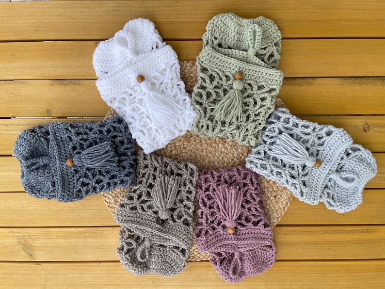 May include: Six crocheted bags with wooden beads and tassels in various colors, including white, gray, green, brown, and pink. The bags are arranged in a circle on a wooden surface.