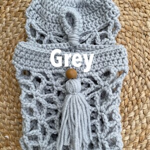 May include: Gray crocheted bag with a wooden bead and tassel. The bag has a geometric pattern and is made with a thick yarn.