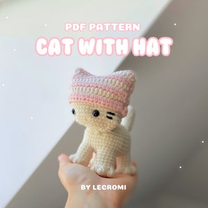 Könnte beinhalten: Ein Häkelmuster für eine weiße Katze mit einem rosa-weiß gestreiften Hut. Das Muster trägt den Titel "PDF PATTERN CAT WITH HAT BY LECROMI".