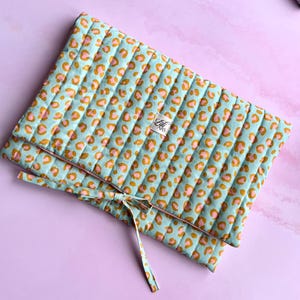 Op de afbeelding: Een gewatteerde clutch met een lichtblauwe achtergrond en een luipaardprint in roze en goud. De clutch is vastgebonden met een bijpassend lint. Het label luidt "Lili & Krs".
