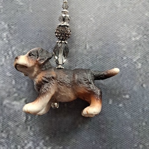 Könnte beinhalten: Ein Schlüsselanhänger zum Thema Hund mit einer kleinen, detaillierten Figur eines Berner Sennenhundes. Der Hund ist in Braun-, Schwarz- und Weißtönen bemalt. Der Schlüsselanhänger enthält einen silberfarbenen Verschluss und dekorative Perlen.