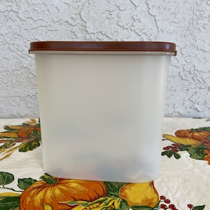 May include: A clear plastic storage container with a brown lid. The container is oval shaped and has a smooth surface.