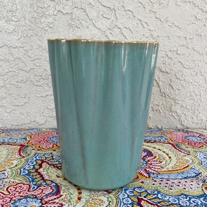 May include: A light blue ceramic planter with a fluted design. The planter has a slightly scalloped rim.