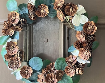A handmade natural pine cone wreath. This wreath is made of pinecones picked by me and adorned with silk eucalyptus. Lovely on any door.