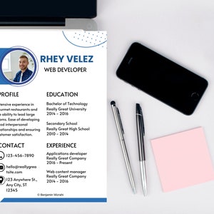 May include: A professional resume template with a blue and white design. The resume includes the name Rhey Velez, contact information, and sections for profile, education, and experience. A laptop, phone, pens, and a sticky note are also visible.