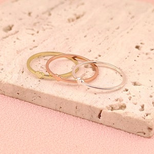 May include: Three thin gold rings stacked on top of each other. The top ring is gold, the middle ring is rose gold, and the bottom ring is silver.