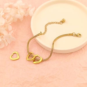 May include: Gold chain bracelet with three heart charms, each engraved with a name: Alex, Robin, and Nadia.