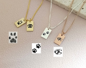 May include: Three necklaces with rectangular pendants featuring paw prints. The necklaces are gold, silver, and rose gold. The pendants are engraved with paw prints.