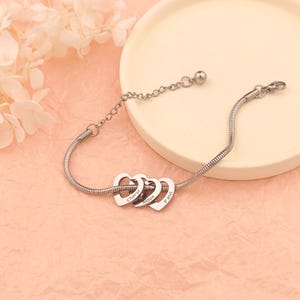 May include: Silver chain bracelet with three interconnected heart charms, each engraved with a name: Cheryl, Alison, and Paul.
