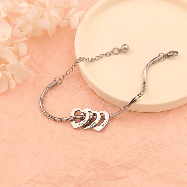May include: Silver chain bracelet with three interconnected heart charms, each engraved with a name: Cheryl, Alison, and Paul.
