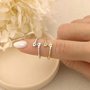 May include: Two open-ended rings featuring heart-shaped terminals. One ring is silver-toned with the letters W and A engraved on the hearts. The second ring is gold-toned with the letters H and K engraved on the heart-shaped ends of the band.