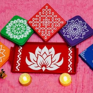 May include: A collection of colorful, square coasters and a rectangular tray with a lotus flower design. The coasters are orange, green, red, purple, and blue, each with a unique white pattern. Two lit candles are at the bottom.
