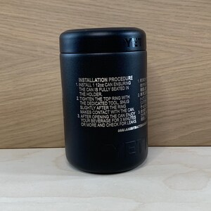 May include: A black cylindrical beverage holder with the brand name "YETI" visible. The product has instructions printed on the side, including how to install a 12oz can. The holder is designed to keep beverages cold.