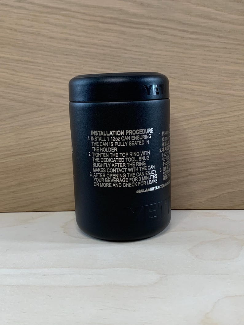 May include: A black cylindrical beverage holder with the brand name "YETI" visible. The product has instructions printed on the side, including how to install a 12oz can. The holder is designed to keep beverages cold.