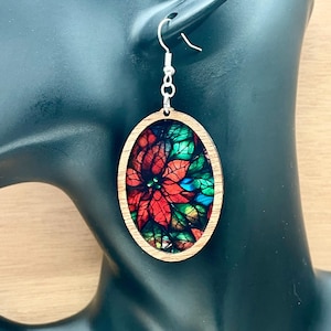 May include: Oval wooden earrings featuring a stained glass style poinsettia design in shades of red, green, and blue.