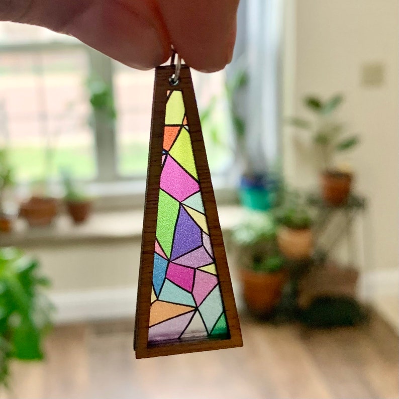May include: A wooden triangle earring with a stained glass design featuring pink, purple, green, blue, and orange colors.
