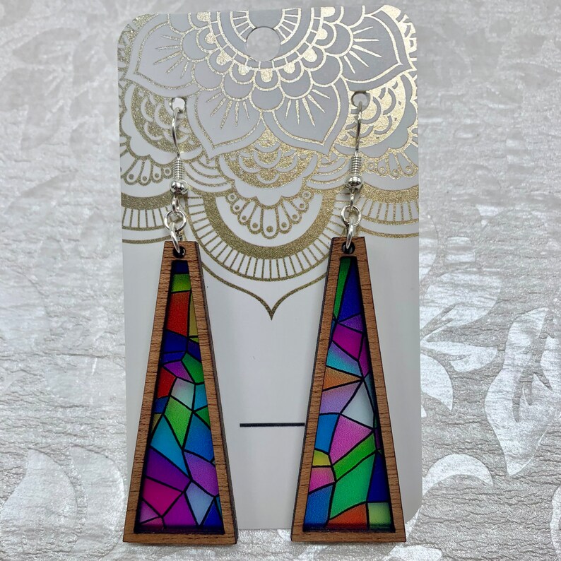 May include: A pair of wooden earrings with a stained glass design. The earrings are shaped like triangles and have a silver hook.
