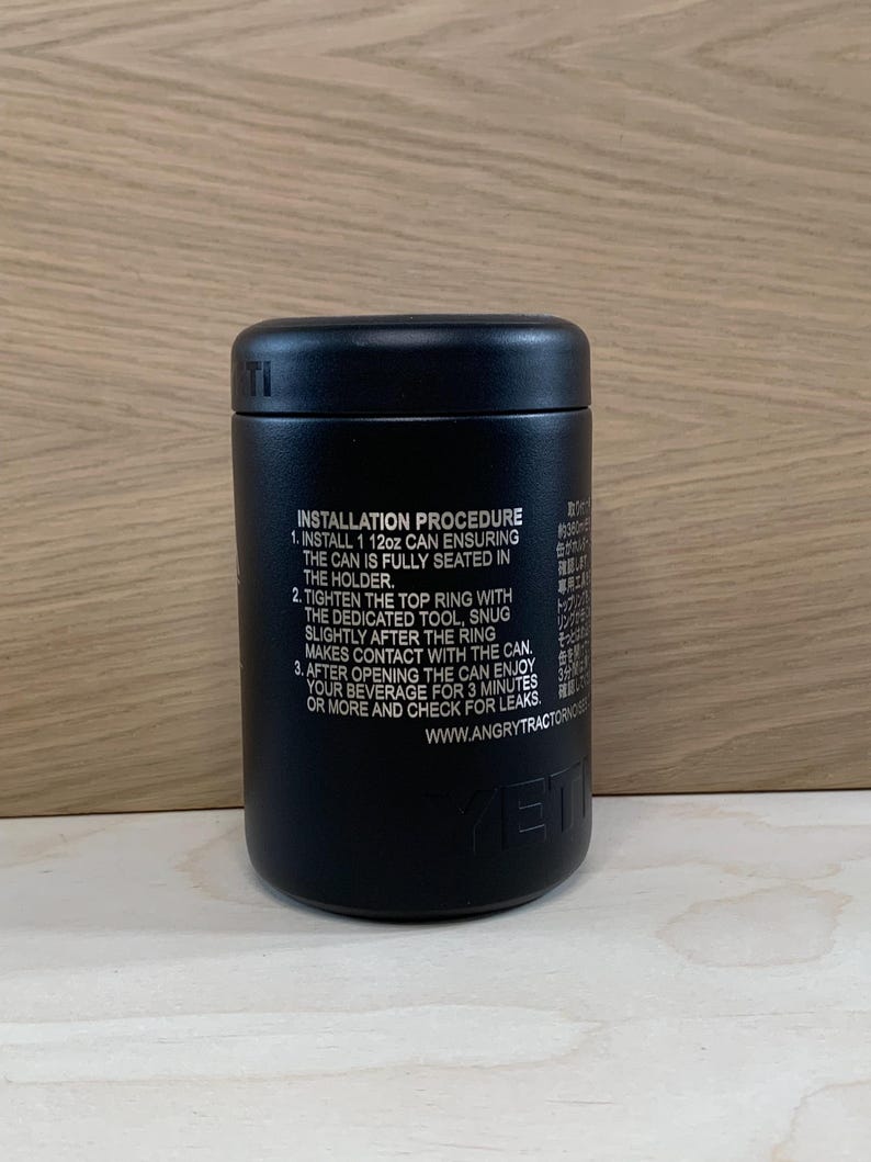 May include: A black insulated can holder with the text "INSTALLATION PROCEDURE" and instructions. The holder is cylindrical and features the brand name "YETI" at the bottom. The holder is designed to hold a 12oz can.