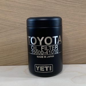 May include: A black YETI oil filter container with the Toyota logo and text "OIL FILTER 15600-41010 MADE IN JAPAN". The container is cylindrical and sits on a light wood surface.