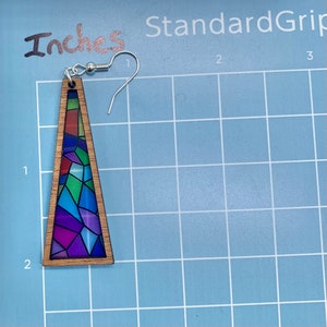 May include: A pair of wooden triangle earrings with a stained glass design featuring a variety of colors, including blue, green, purple, and red. The earrings are approximately 2 inches long.