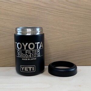 May include: Black YETI tumbler with a silver rim and a separate black ring. The tumbler features the word "TOYOTA" and "OIL FILTER 15600-41010" in white text. The text "MADE IN JAPAN" is also visible.