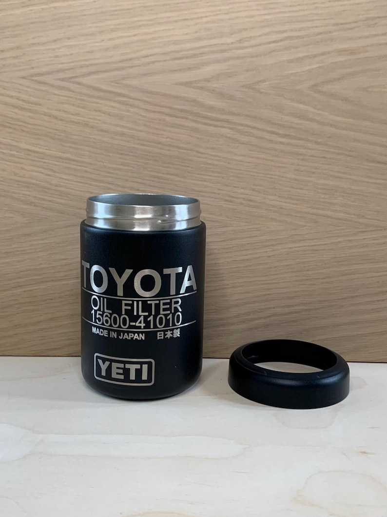 May include: A black YETI tumbler with a silver rim and a black rubber base. The tumbler features the Toyota logo and "OIL FILTER 15600-41010" printed in white. The text "MADE IN JAPAN" and Japanese characters are also visible.