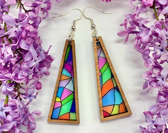 May include: A pair of colorful, geometric, wooden earrings with a stained glass design. The earrings are triangular in shape and have silver hooks.