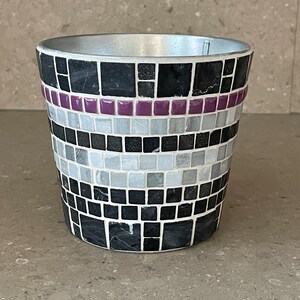 Könnte beinhalten: Ein schwarzer und weißer Mosaik-Pflanztopf mit einem Band aus violetten Fliesen am oberen Rand.
