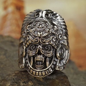 May include: A bronze ring with a detailed skull design. The skull is wearing a crown with intricate carvings. The ring is a statement piece with a gothic aesthetic.