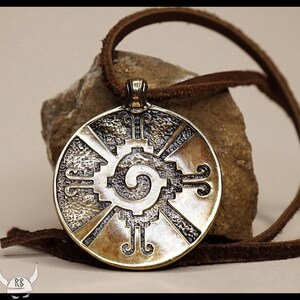 May include: A round, bronze pendant with a detailed design of a spiral and geometric shapes. The pendant is on a brown leather cord.