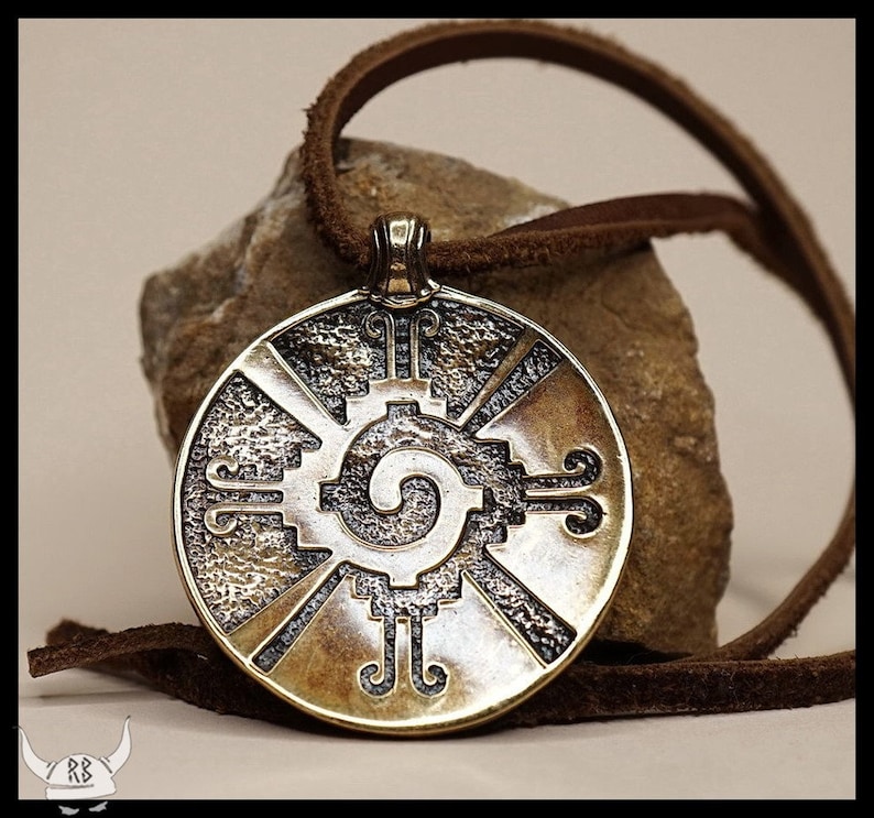 May include: A round, bronze pendant with a detailed design of a spiral and geometric shapes. The pendant is on a brown leather cord.