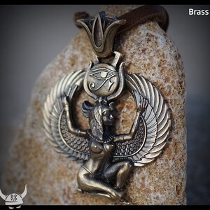 Puede incluir: Un colgante de lat&oacute;n que representa a la diosa egipcia Isis con las alas extendidas. El colgante incluye el s&iacute;mbolo del Ojo de Horus y un dise&ntilde;o de flor de loto.