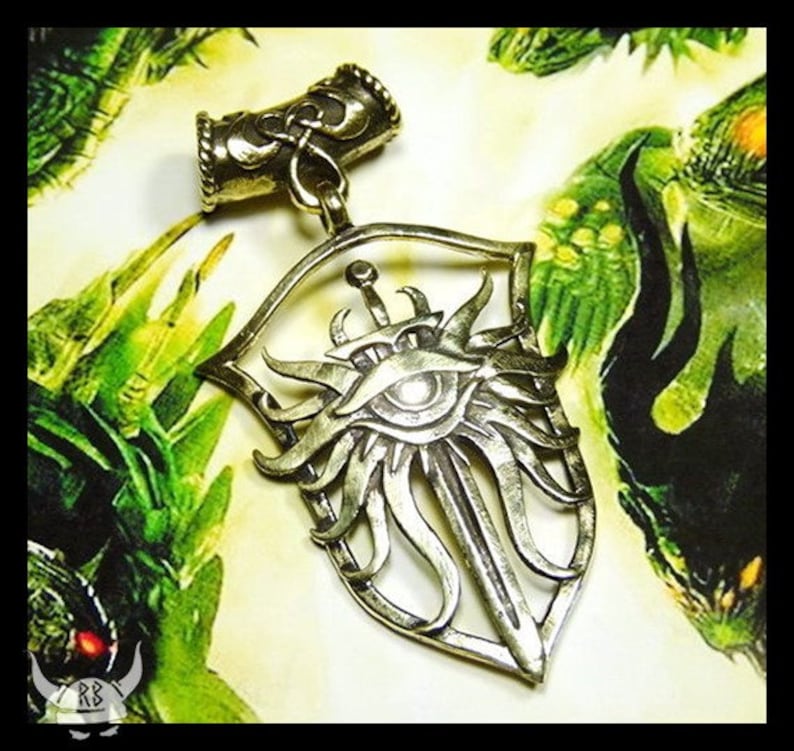 May include: A silver pendant featuring a shield with a sword and an eye in the center. The shield is surrounded by a decorative design of swirling lines. The pendant is attached to a silver chain.