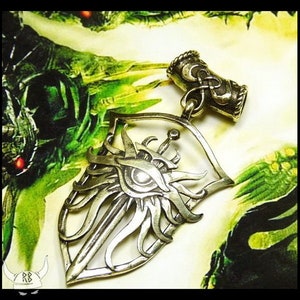 May include: A silver pendant in the shape of a shield with a sword and an eye inside. The pendant is on a green and brown background.