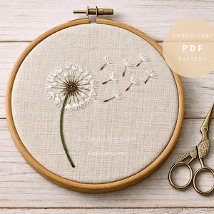 May include: Embroidered dandelion design in a wooden hoop. The artwork features a white dandelion with seeds blowing away, a green stem, and the text "Embroidery PDF Pattern". Gold-colored scissors are placed to the right.