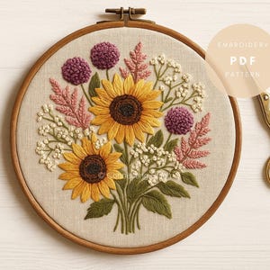 May include: Embroidered floral design featuring two sunflowers, purple pom-pom flowers, and pink and white foliage. The embroidery is set in a wooden hoop. A pair of gold scissors is on the right. The text "EMBROIDERY PDF PATTERN" is on the right.