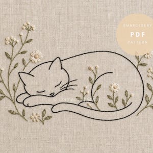 Puede incluir: Un patrón de bordado sobre tela beige claro con una ilustración de línea negra de un gato durmiendo rodeado de tallos verdes bordados y pequeñas flores blancas. El texto EMBROIDERY PDF PATTERN está impreso en un círculo beige.