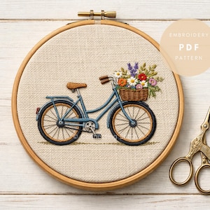 Puede incluir: Un bastidor de bordado con un diseño cosido detallado de una bicicleta azul con una cesta de flores. El bordado está sobre una tela neutra, con un aro de madera. El texto "EMBROIDERY PDF PATTERN" está en un círculo. Tijeras doradas a la derecha.