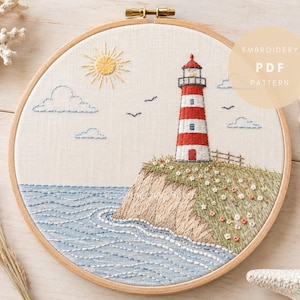 May include: Embroidered lighthouse design in a wooden hoop. The scene depicts a red and white striped lighthouse on a grassy cliff, with blue water, clouds, and a yellow sun. The text "EMBROIDERY PDF PATTERN" is visible.
