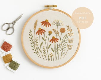 May include: An embroidery hoop with a floral design featuring orange and yellow flowers and green leaves. The text "EMBROIDERY PDF PATTERN" is on the upper right. Scissors and spools of thread in orange, yellow, and green are on the left.