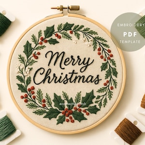 Könnte beinhalten: Bestickter Weihnachts-Stickrahmen mit dem Schriftzug "Merry Christmas" in schwarzer Schrift, umgeben von einem Kranz aus grünen Stechpalmenblättern und roten Beeren. Das Design befindet sich auf beigem Stoff, mit Garnrollen in Grün, Rot und Creme.