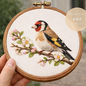 Op de afbeelding: Een ronde houten borduurring met een stoffen paneel waarop een gedetailleerde, met draad geborduurde putter op een bloeiende tak is afgebeeld. De vogel heeft een rood, zwart en bruin verenkleed. De tekst EMBROIDERY PDF PATTERN is zichtbaar.