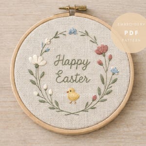 May include: Embroidered hoop art featuring a floral wreath design. The words "Happy Easter" are stitched in the centre, with a small yellow chick below. The design includes white, pink, and blue flowers. The text "Embroidery PDF Pattern" is in a circle.