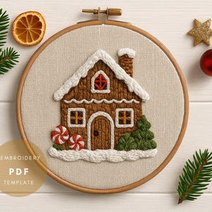 Può includere: Casa di pan di zenzero ricamata in un cerchio di legno. La casa marrone ha accenti di neve bianca, una finestra rossa e un camino. Due caramelle rosse e bianche e un albero verde sono sul davanti. Una fetta d'arancia secca, una stella dorata e una palla rossa sono vicine.