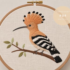 May include: An embroidery hoop containing a fabric panel with a stitched hoopoe bird perched on a branch. The bird has orange plumage, a crest, and black and white striped wings. The text EMBROIDERY PDF PATTERN is visible in the upper right corner.
