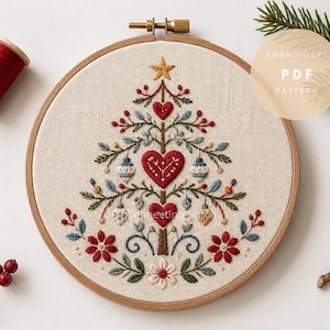 以下が含まれることがあります： 刺繍されたクリスマスツリーのデザインが施された布パネルが入った円形の木製刺繍枠。ツリーには赤いハート、青と白のオーナメント、黄色い星があしらわれています。画像内のテキストには「EMBROIDERY PDF PATTERN」と書かれています。